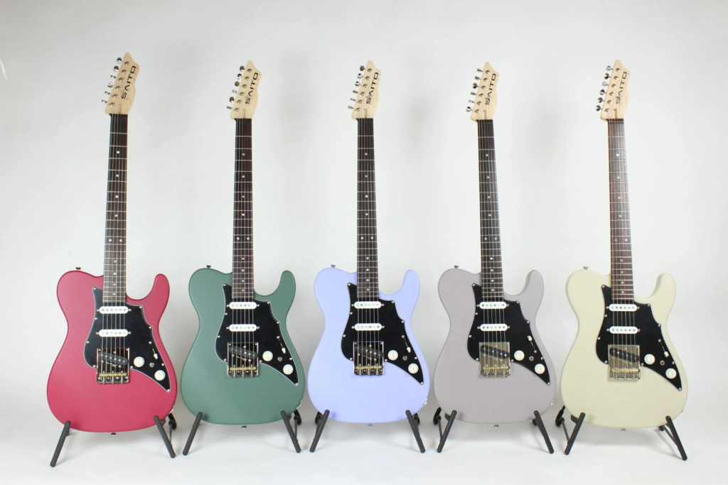 Five Saito Guitars offset electric guitars in red, green, light blue, gray, and cream finishes with black pickguards and single-coil pickups displayed on stands against a white background.
