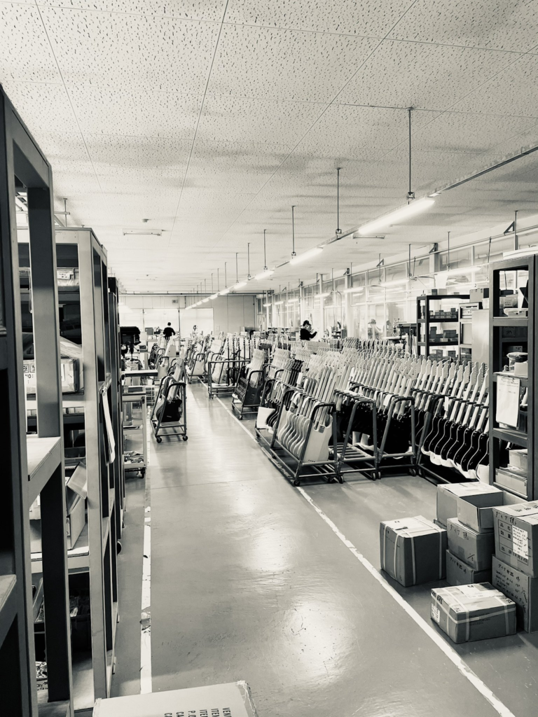 Interior of a Japanese guitar factory showing rows of unfinished electric guitar bodies on racks along a production line.