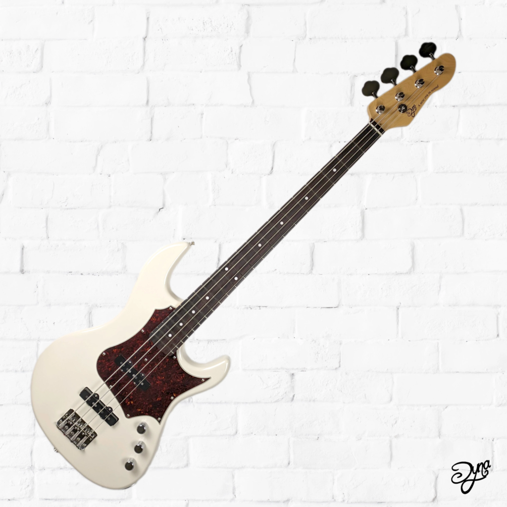 Dyna Gakki VL Standard Vintage electric bass in cream finish with tortoiseshell pickguard, split single-coil pickup, and four-string configuration against a white brick background.