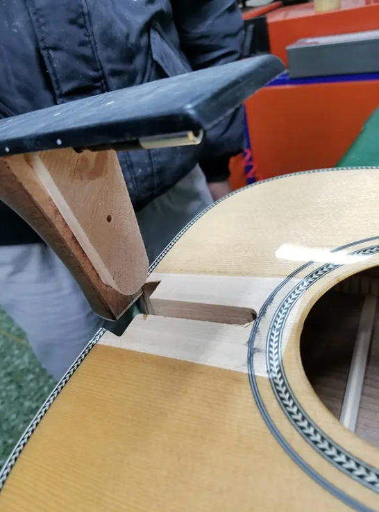 Close-up of a dovetail neck joint being fitted to a Headway acoustic guitar body, showing the oversized tenon and mortise